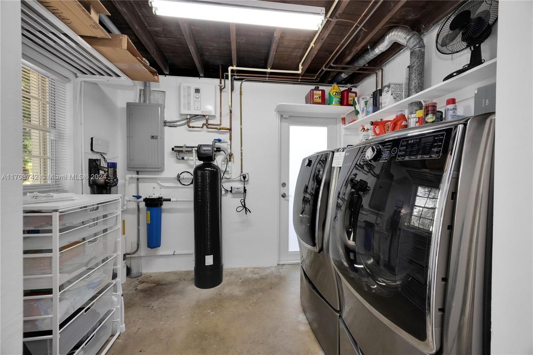 Utility Room with new full-size washer/dryer, tankless hot water heater and water filtration system with exit door to backyard.