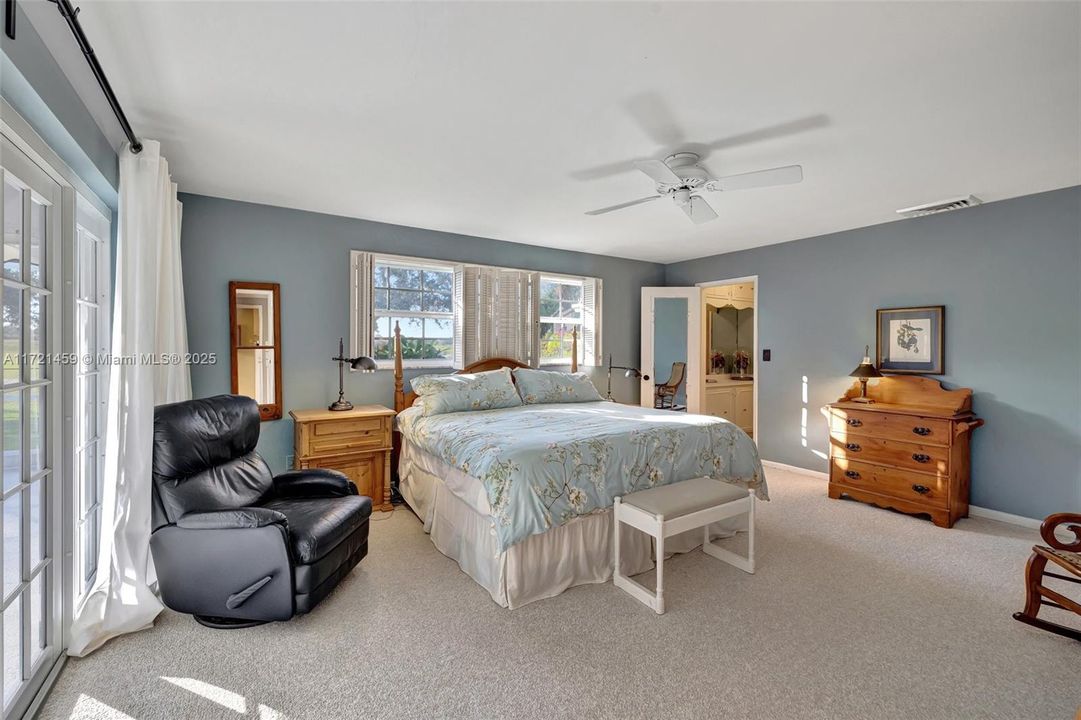 Primary Bedroom w/ windows to the golf course behind, and French doors which lead to the pool area. To the right is the walk in dressing area / oversized closet