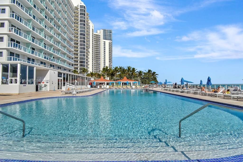 Resort-style swimming pool overlooking the beach, surrounded by lounge chairs and palm trees—true Sunny Isles luxury.