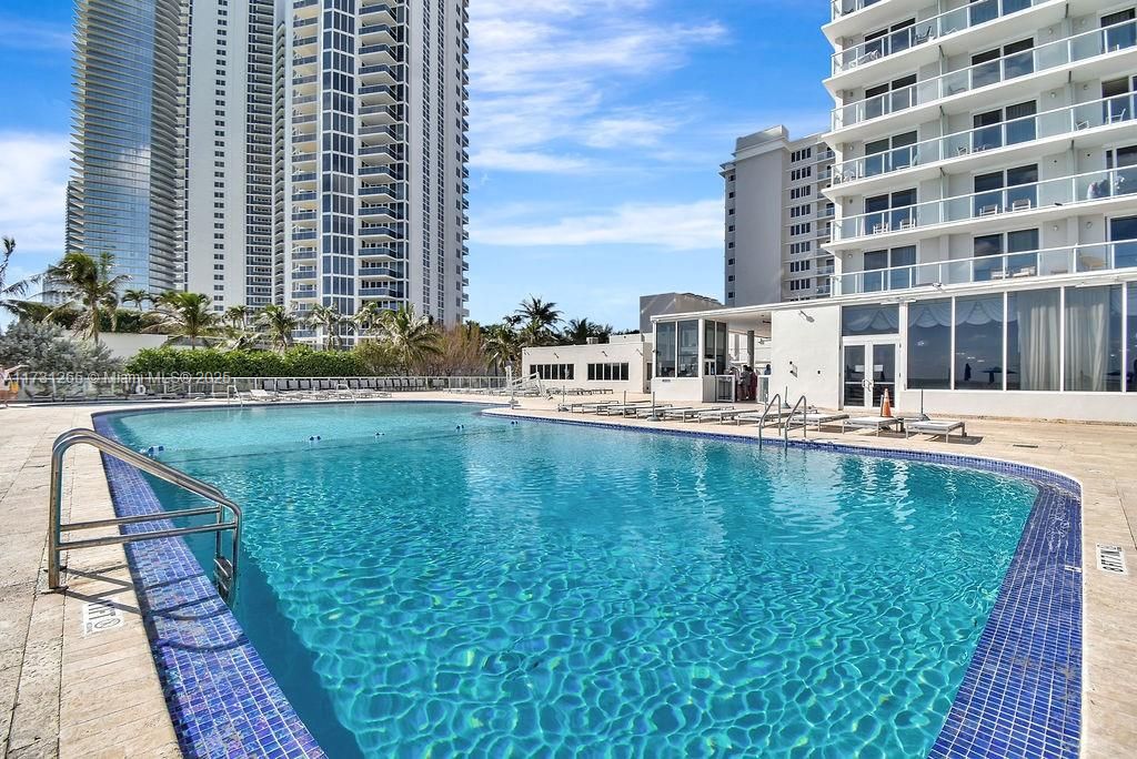 Resort-style swimming pool overlooking the beach, surrounded by lounge chairs and palm trees—true Sunny Isles luxury.