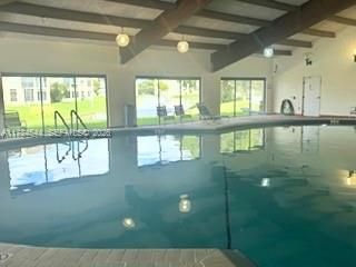 Indoor swimming pool featuring an expansive curved design, exposed wooden beams, multiple glass sliding doors, and surrounding tile decking