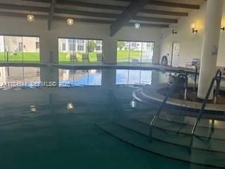 Indoor pool featuring floor-to-ceiling windows, exposed timber ceiling beams, integrated circular spa, and built-in wall lighting