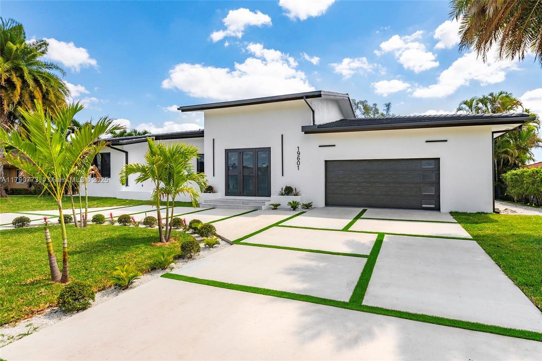This brand-new modern contemporary home features a flat concrete tile roof, block-paved circular driveway, and impact-resistant windows and doors for lasting beauty and protection.