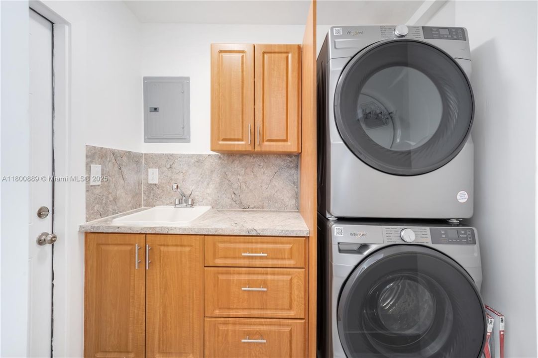 Laundry room with stacked washer/dryer, utility sink and tankless water heater.  Door leading to the outside and backyard.