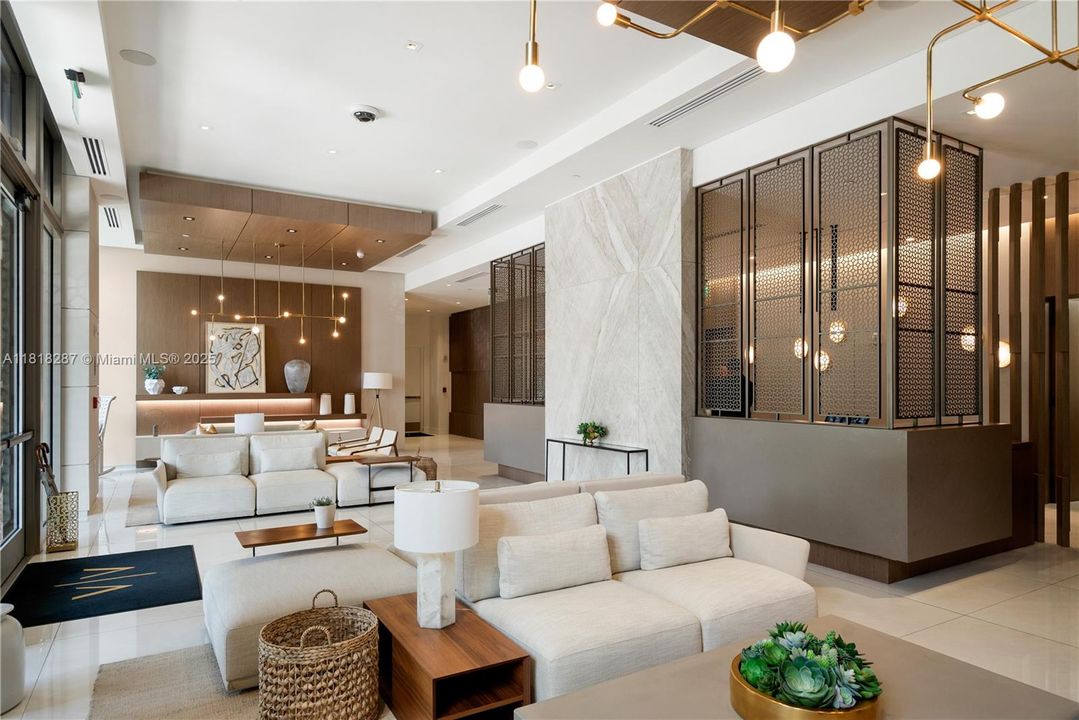 Sophisticated lobby with custom stonework, wood accents, and contemporary lighting welcoming residents and guests in timeless Coral Gables style.
