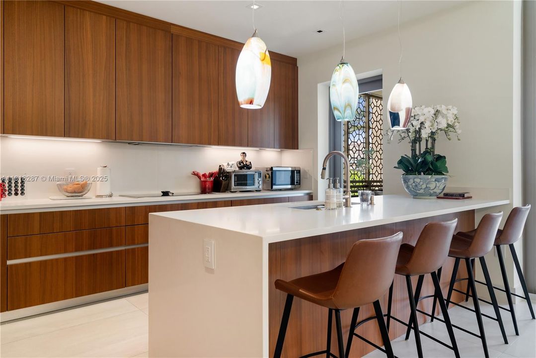 Sleek gourmet kitchen with custom walnut cabinetry, quartz island, and pendant lighting creating a warm, elegant atmosphere.