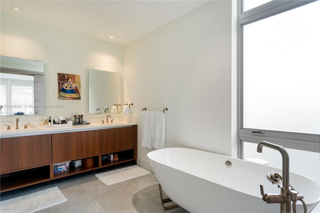 Modern en-suite bath offering a double vanity with sleek wood cabinetry, warm fixtures, and clean contemporary finishes throughout.