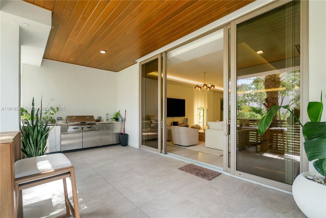 Fully equipped summer kitchen with stainless-steel cabinetry, small fridge and grill, seamlessly connecting the indoor and outdoor living spaces.