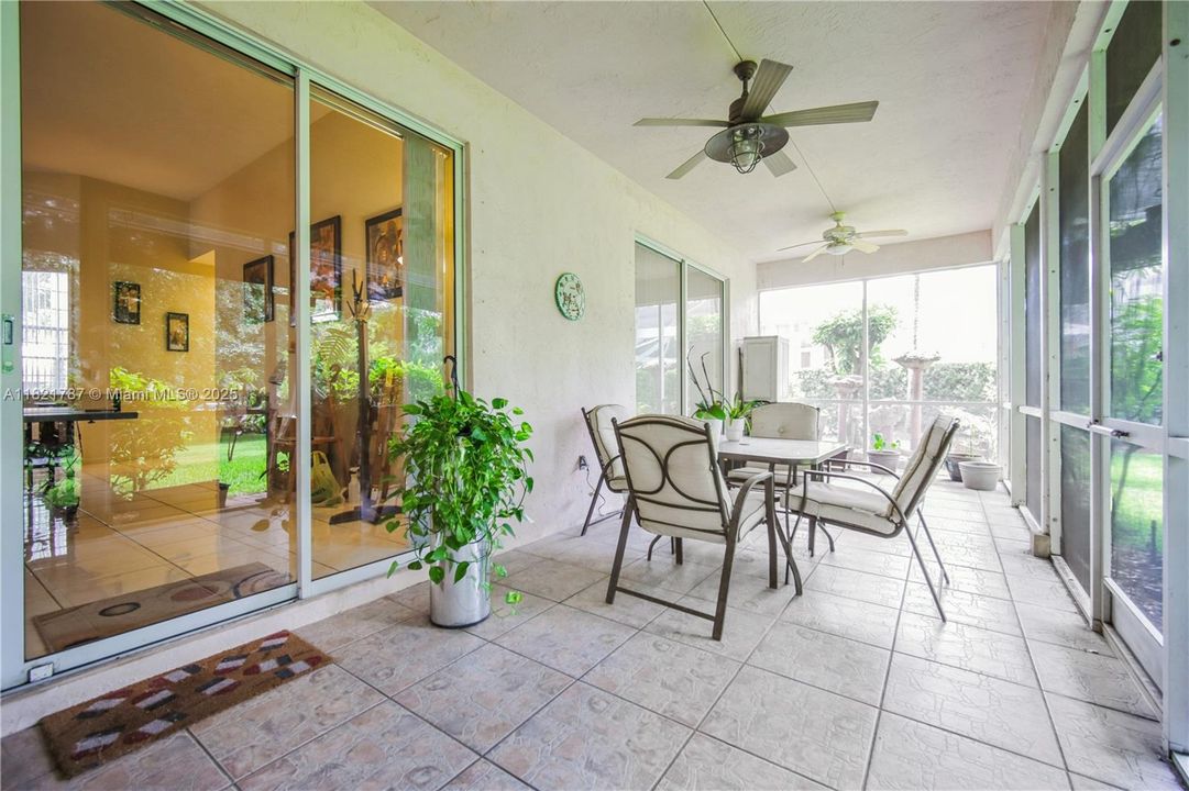Wide, screened-in patio space with ceiling fan & view of lovely plants, flowers & adjacent water fountain.