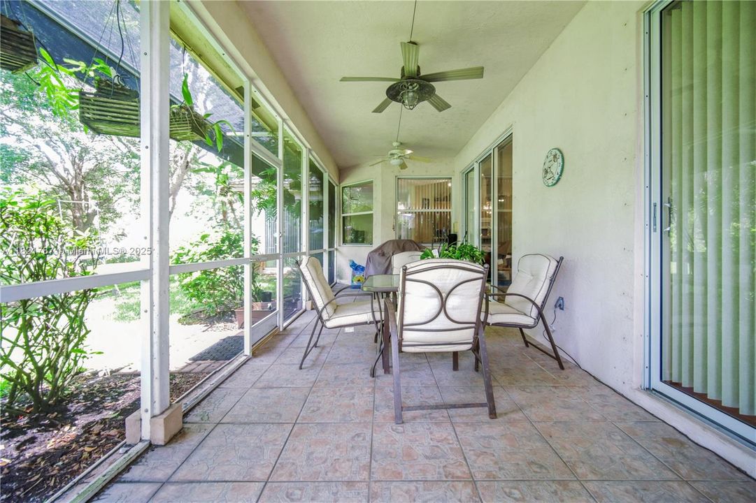 Wide, screened-in patio space with ceiling fan & view of lovely plants, flowers & adjacent water fountain.