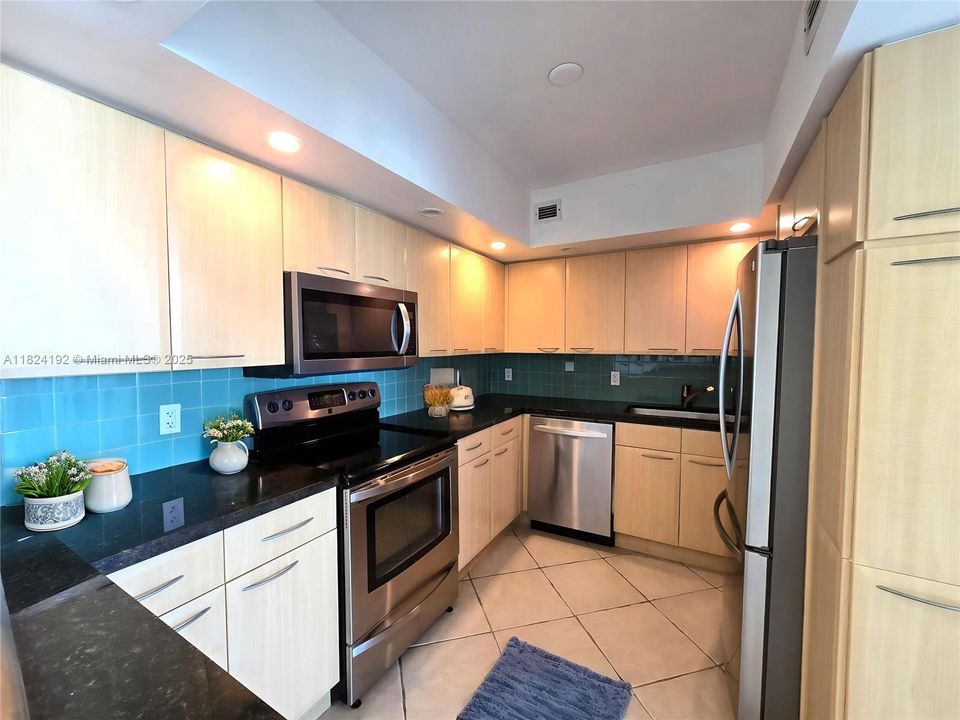 Spacious and functional kitchen featuring sleek granite countertops, modern stainless steel appliances, and abundant cabinet storage. The U-shaped layout maximizes prep space and efficiency, while under-cabinet lighting and a passthrough window create a bright and welcoming cooking environment.