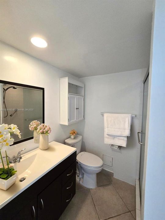 Guest bathroom featuring a modern vanity with ample counter space, large wall-mounted mirror, and a walk-in shower with glass door enclosure. Neutral tile flooring and recessed lighting provide a clean, functional look.