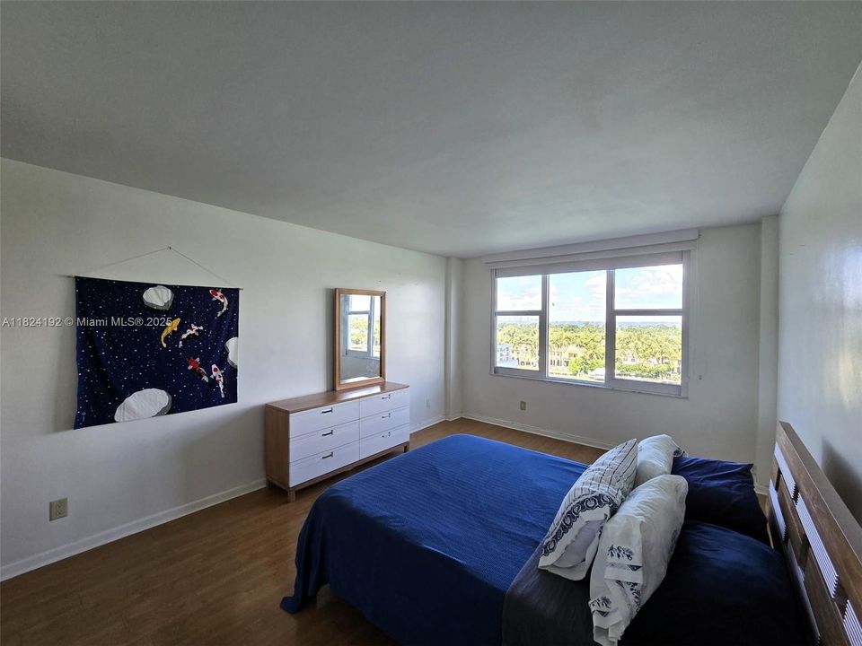 Spacious and bright bedroom with large windows offering lush green views and abundant natural light. Features wood-look flooring, clean lines, and a layout that easily accommodates multiple configurations. Ideal for use as a primary or guest suite