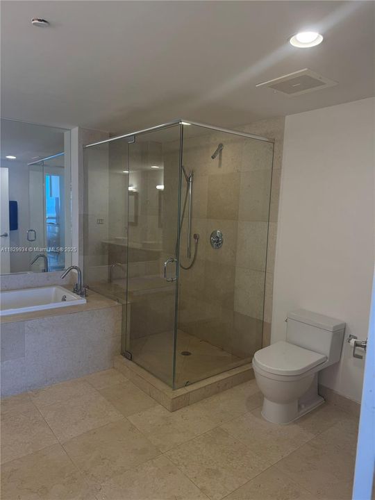 Spacious primary bath featuring a glass-enclosed shower, soaking tub, and sleek stone finishes for a spa-like feel.