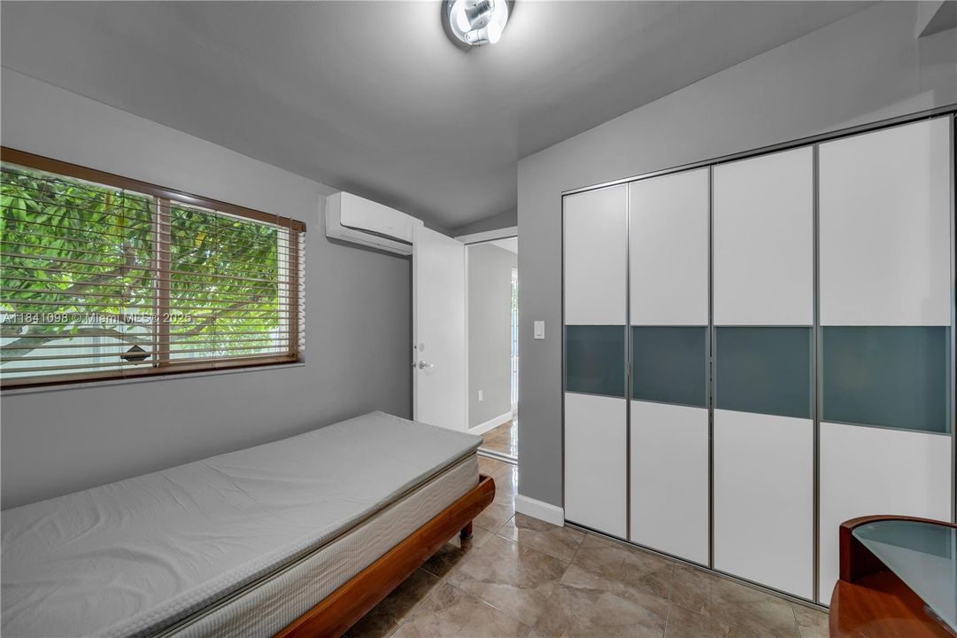 Has its own mini-split A/C unit and a reach-in sliding-door closet featuring solid white and frosted glass panels. Closet offers built-in shelving and drawers for organized storage. Room connects to an adjacent bedroom through a convenient sliding door—perfect for siblings or flexible use.