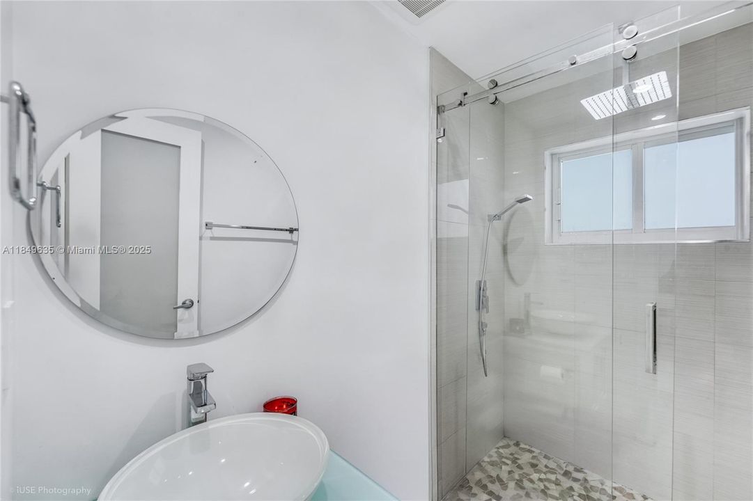 Guest bathroom includes a modern round mirror, vessel sink, and a walk-in shower with neutral stone flooring.
