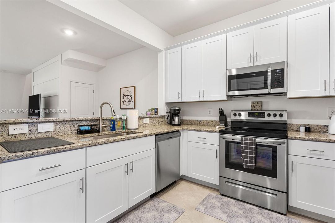 Spacious kitchen boasts granite countertops, stainless steel appliances, deep sink & white shaker cabinets.