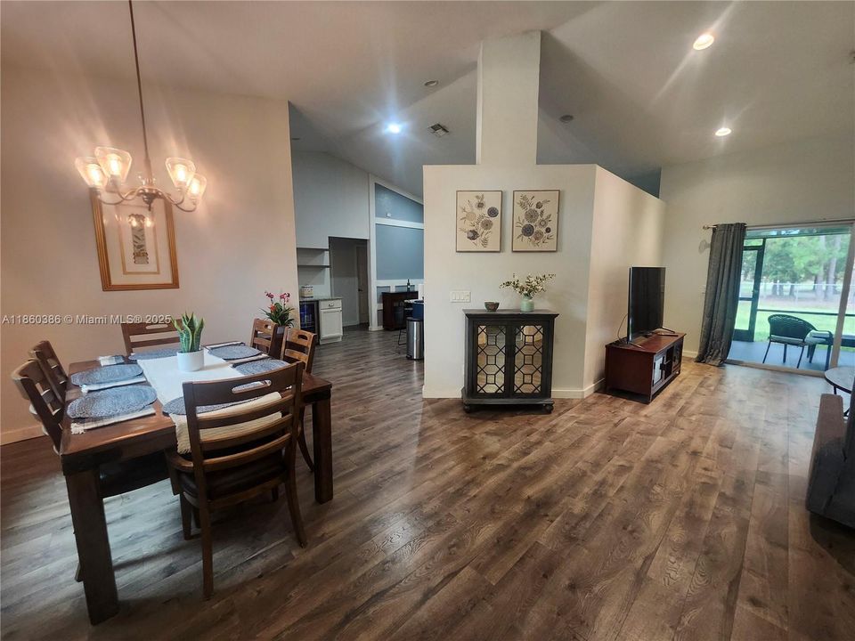 Living & Dining areas with dark wood-type flooring, high vaulted ceilings & beautiful backyard views.
