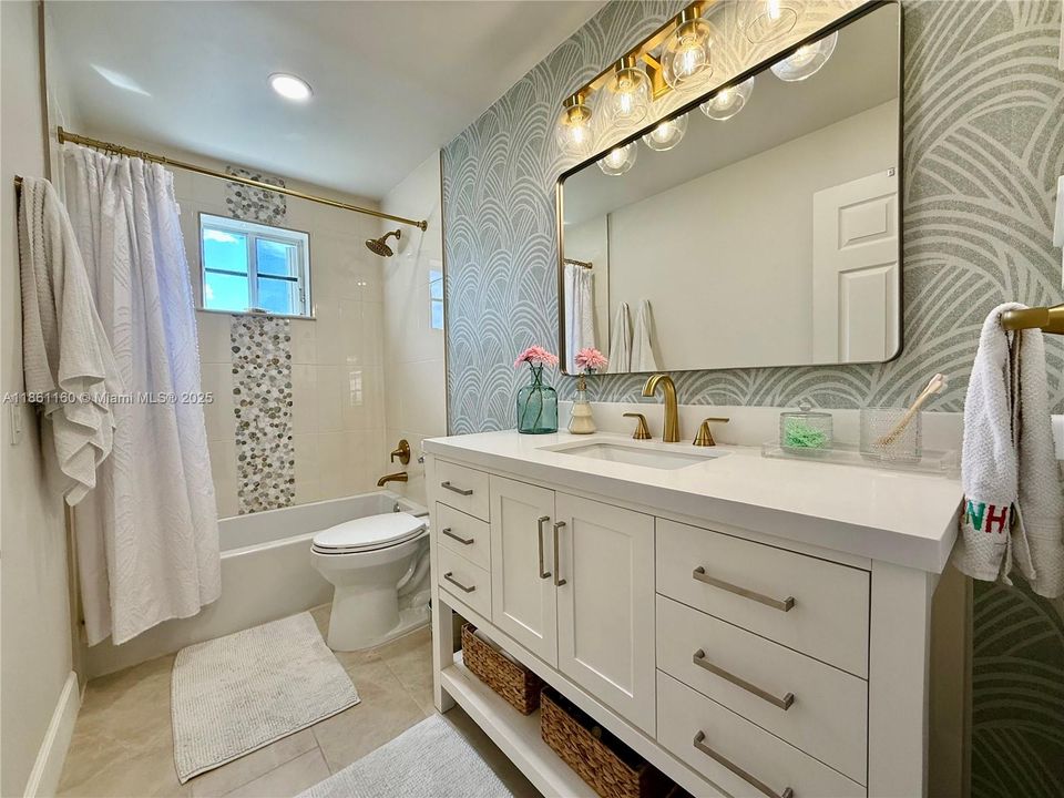 The designer touches continue into the beautifully remodeled second bathroom. This chic space features a stylish modern vanity with ample storage, elegant brushed-gold fixtures, and a sophisticated wallpaper accent wall that adds texture and personality. A crisp, fully updated tub and shower combination completes this impressive and highly functional bathroom.