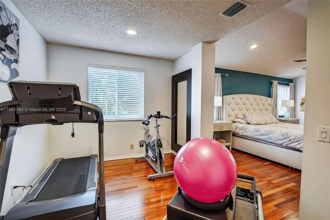 Connected seamlessly to the primary bedroom, this versatile flex space offers endless possibilities. Imagine a private home office, a quiet nursery, a peaceful yoga studio, or a personal fitness area as shown. With its own window providing natural light and rich hardwood floors, this bonus room is ready to adapt to your lifestyle.