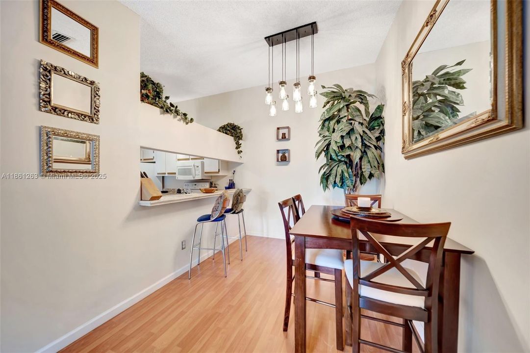 Dining area with modern pendant lighting and wood-style floors, plus a breakfast bar that opens to the kitchen — great for hosting or casual meals.