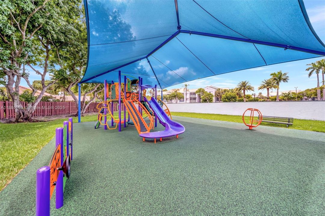 Shaded community playground with soft turf and colorful slides — a great outdoor play area that stays cool under the sun.