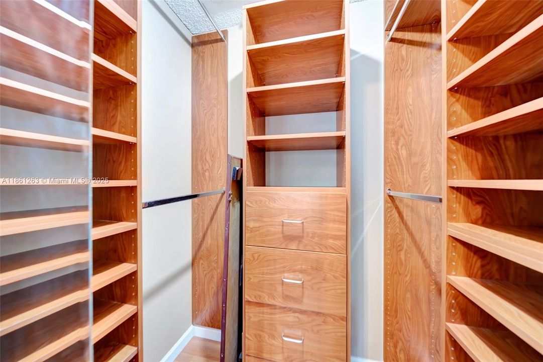 Walk-in closet with custom built-ins, floor-to-ceiling shelving, and three deep drawers — tons of organized storage for clothes, shoes, and accessories. Neutral finishes and wood-style shelving make it feel high-end and move-in ready.