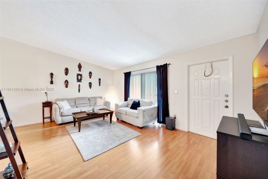 Bright living room with wood-style floors, neutral walls, and sliding glass doors for natural light — a comfortable, open space to relax and entertain.