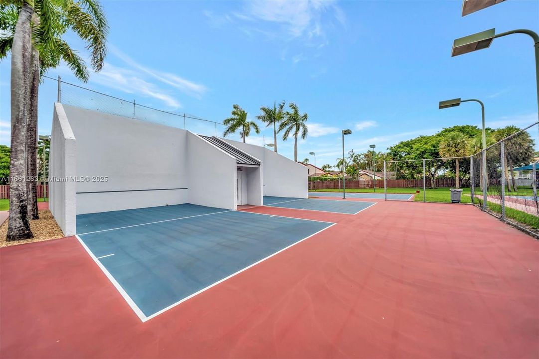 Lighted community tennis courts and practice wall, surrounded by palm trees — great for a quick match or staying active close to home