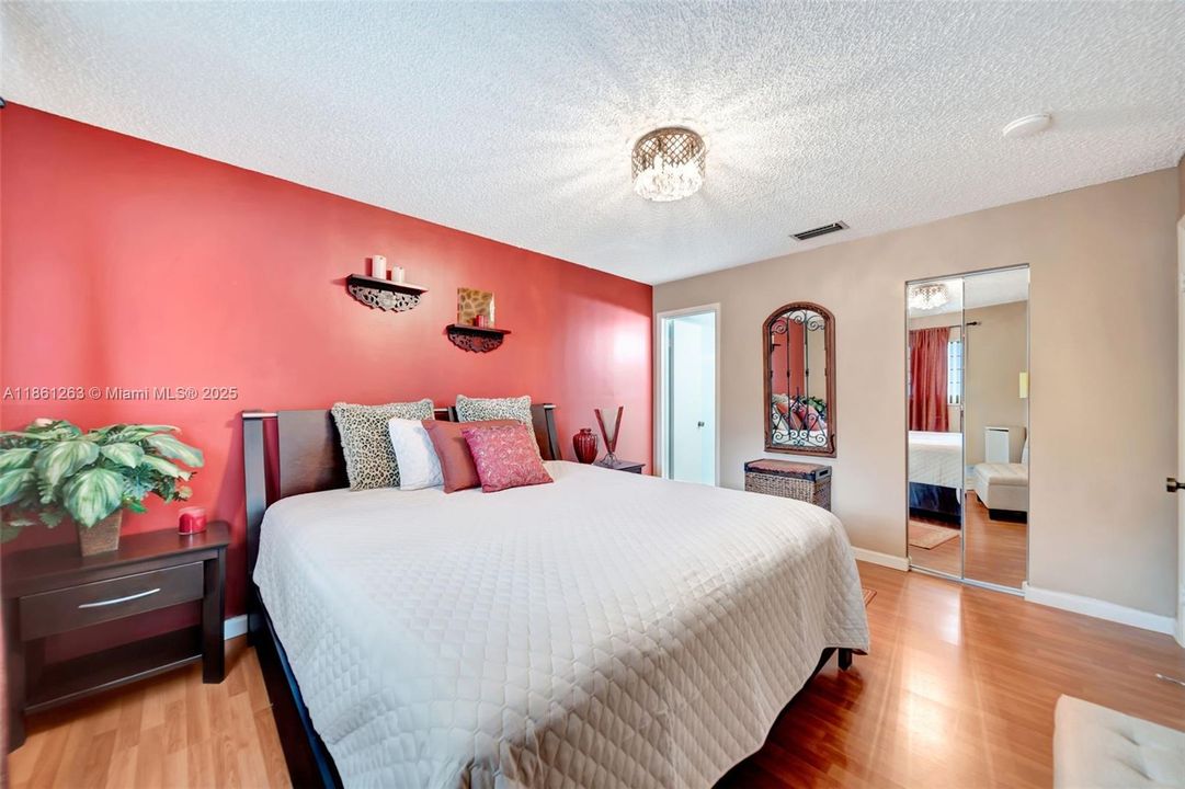 Spacious bedroom with warm wood floors, accent wall, and mirrored closet doors, plus direct access to the bathroom.