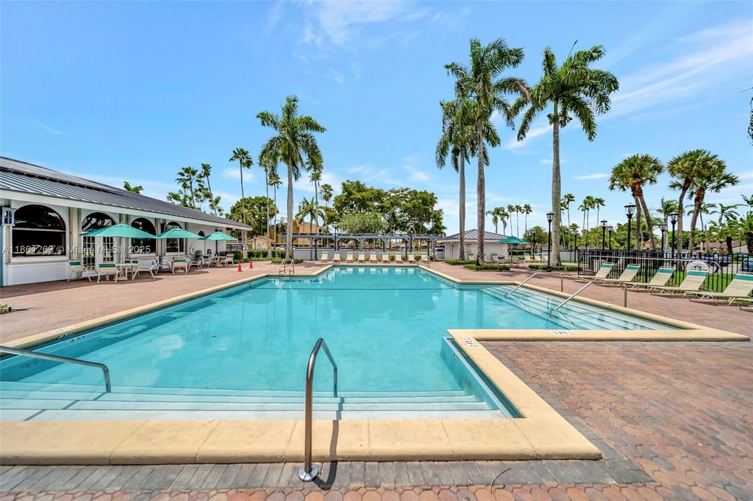Resort-style community pool surrounded by palm trees, sun loungers, and shaded seating areas — perfect for relaxing or spending the day outdoors.