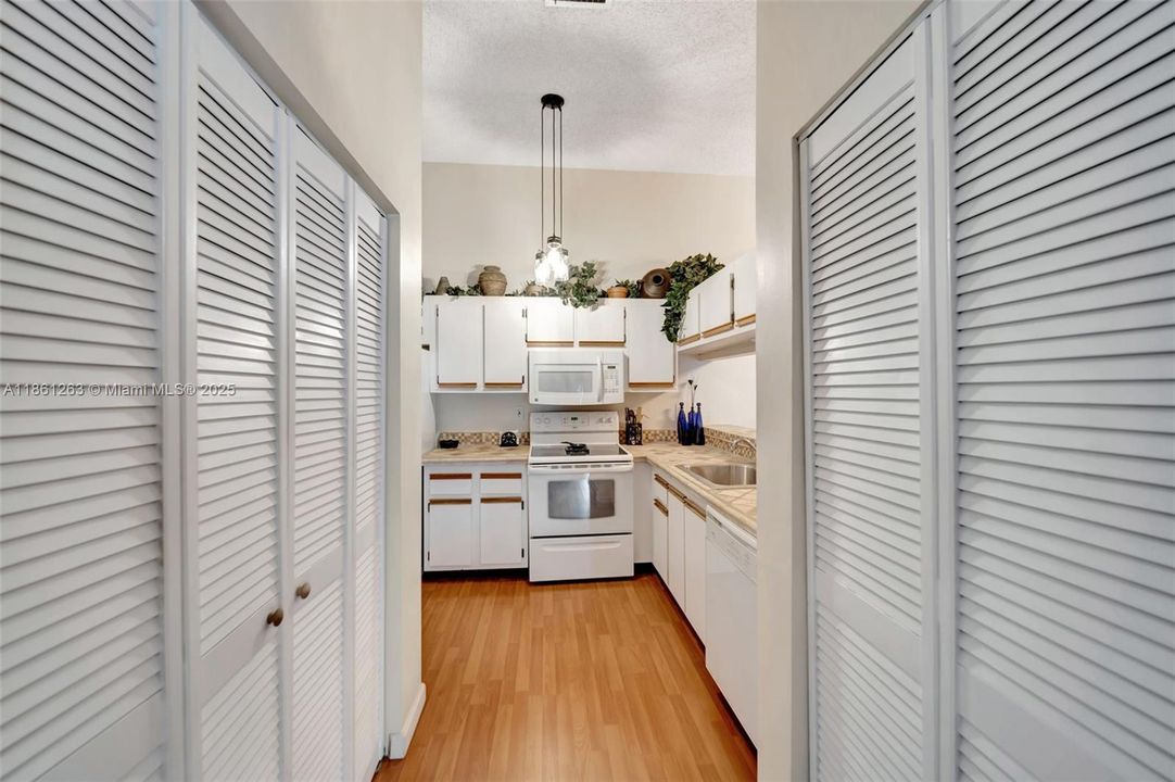 Galley-style kitchen with white cabinets and matching appliances, bar seating, and a pantry-lined entry for extra storage — functional and efficient layout.