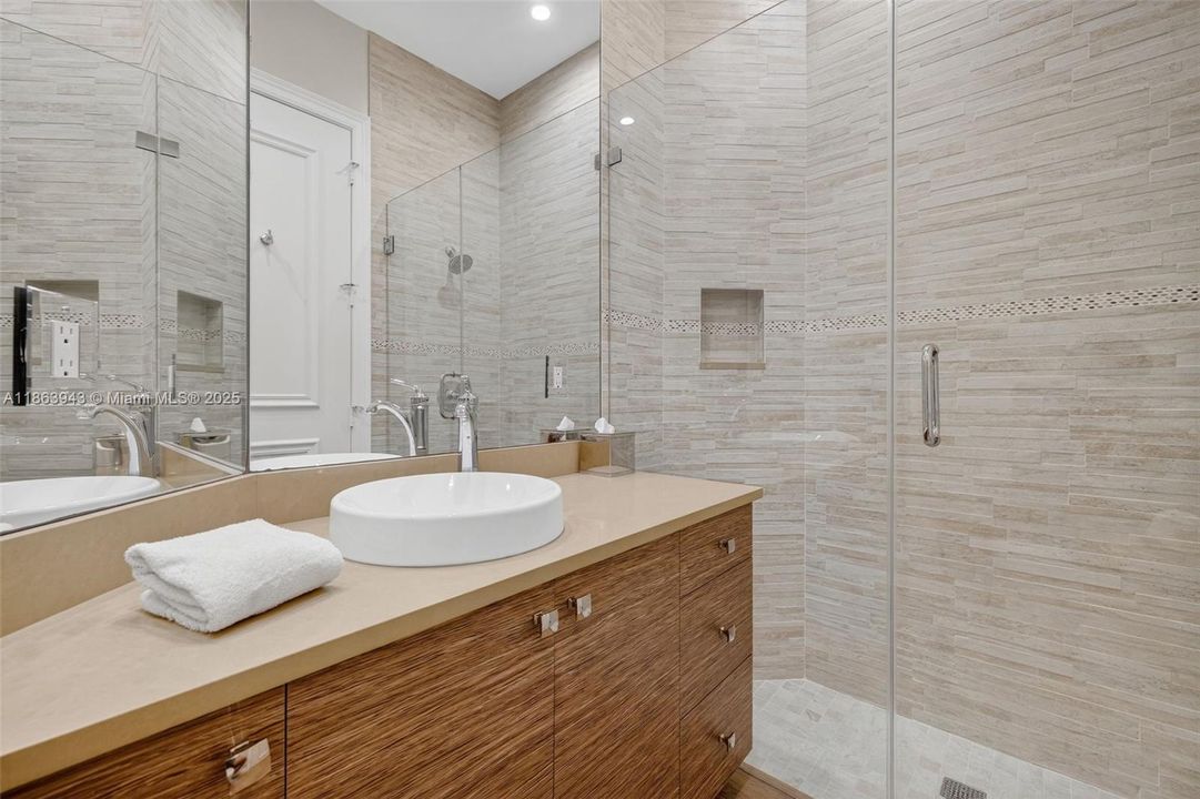 En Suite Guest Bathroom professionally designed by bathroom designer w/ wood grain cabinets, tile to the ceiling and frameless shower doors