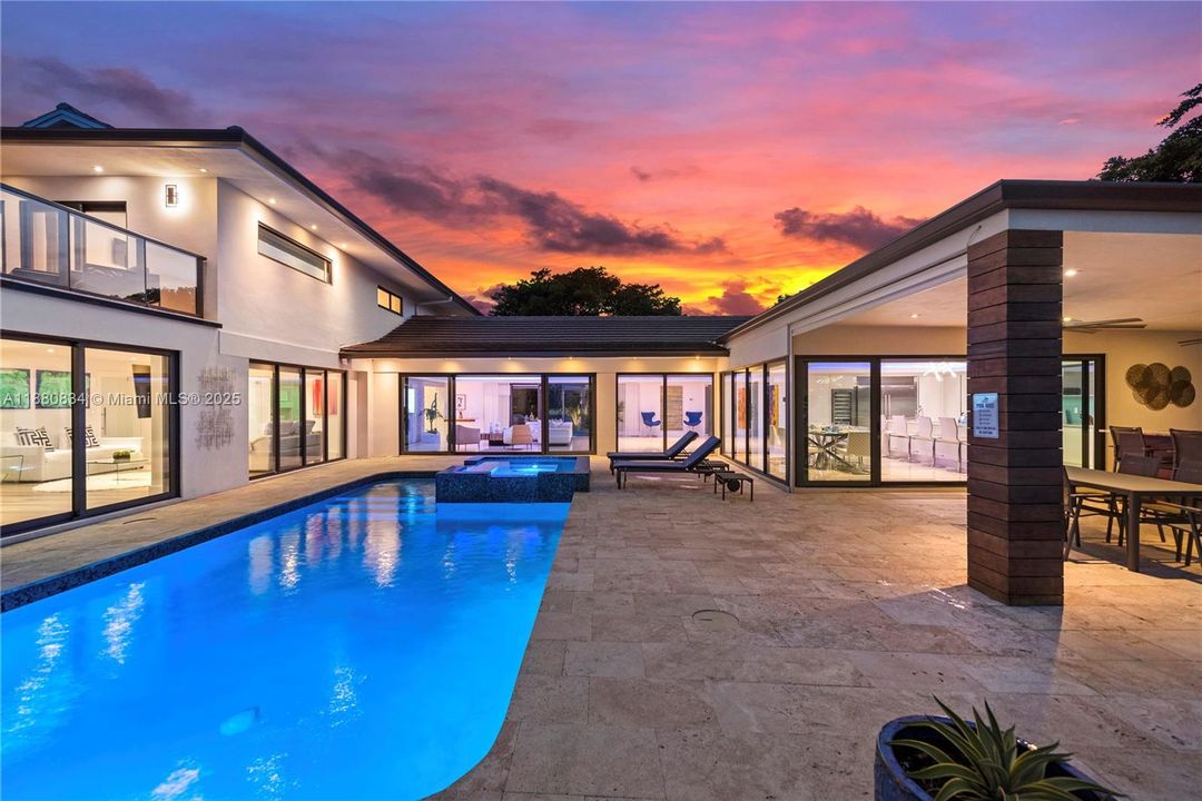 Twilight view of the illuminated house and pool at sunset.