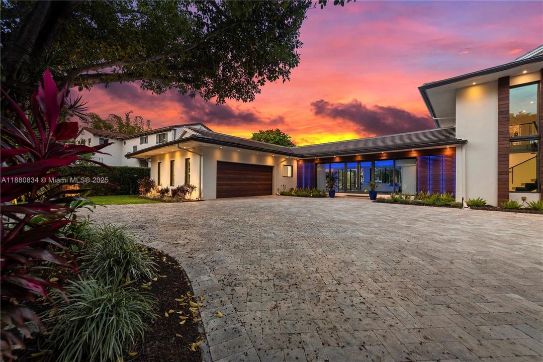 Front exterior of the house with lush landscaping and circular driveway and two car garage