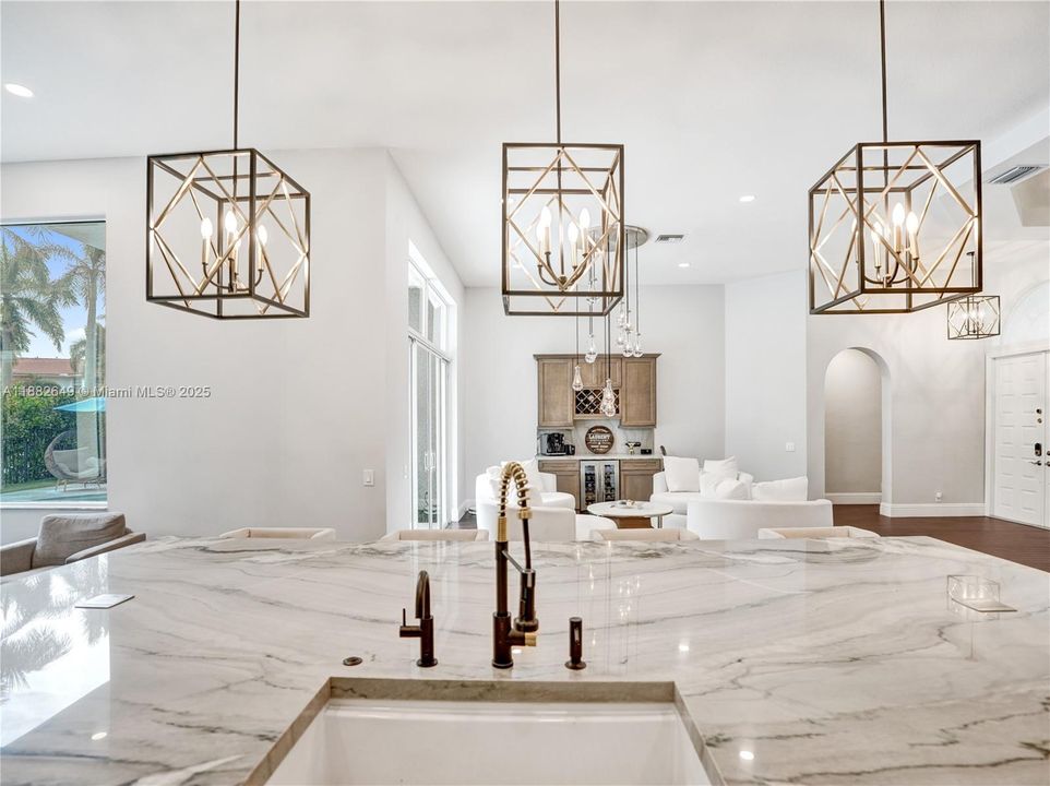 Three stunning modern chandelier light fixtures illuminate the pristine oversized kitchen island