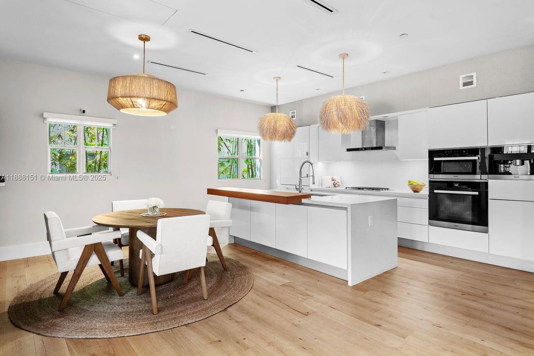 Contemporary open-concept kitchen with white cabinetry, quartz countertops, stainless-steel appliances, and designer lighting.