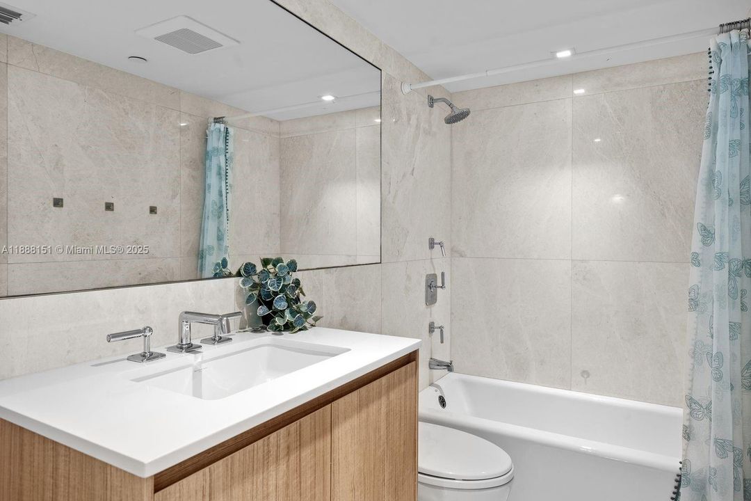 Minimalist guest bath with modern tile, frameless shower, and elegant lighting.