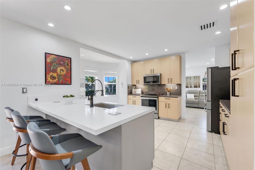 Contemporary kitchen with stainless steel appliances, quartz countertops, breakfast bar, and open flow to dining and living spaces.