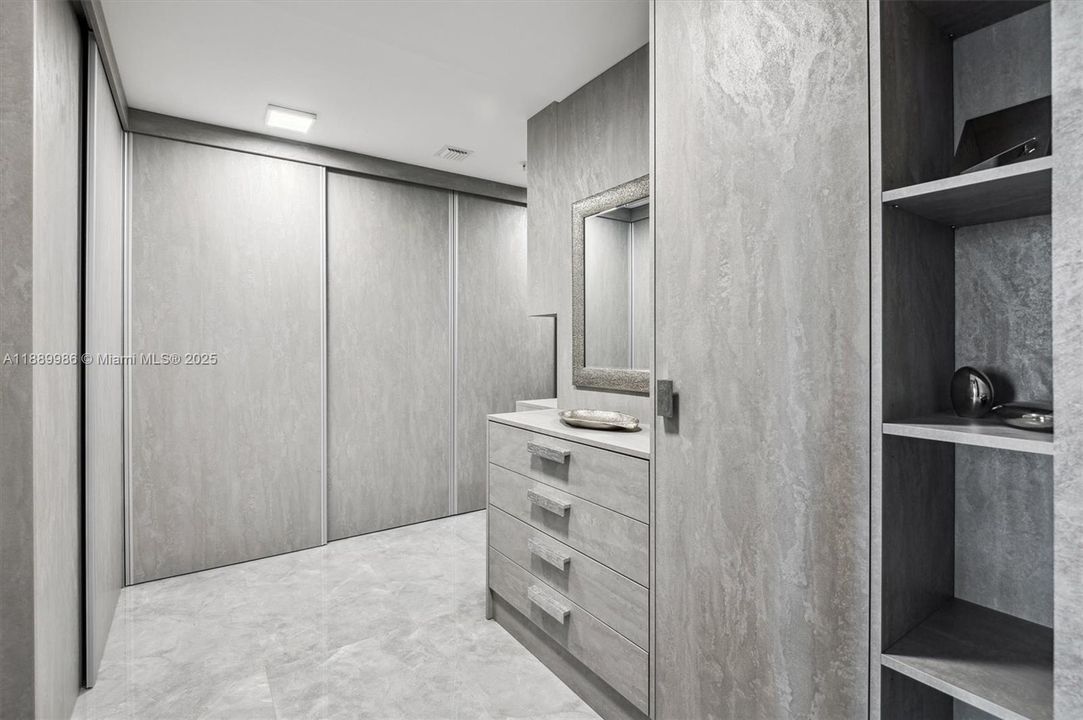 - Primary Spacious L-Shaped Walk-In Closet Custom Built Out Wooden Cabinetry, Display Shelving & Sliding Doors with Michael Aram Hardware.