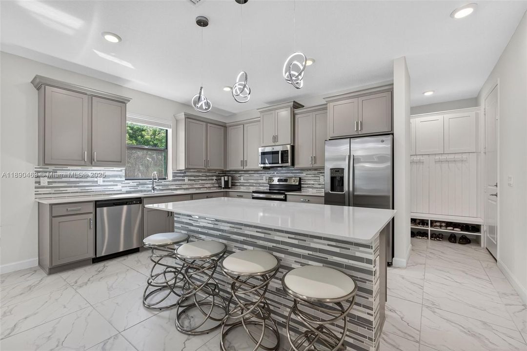Bright, modern kitchen with a huge quartz island, stainless steel appliances, sleek gray cabinetry, and designer pendant lights — plus a built-in mudroom nook with storage to keep everything organized.