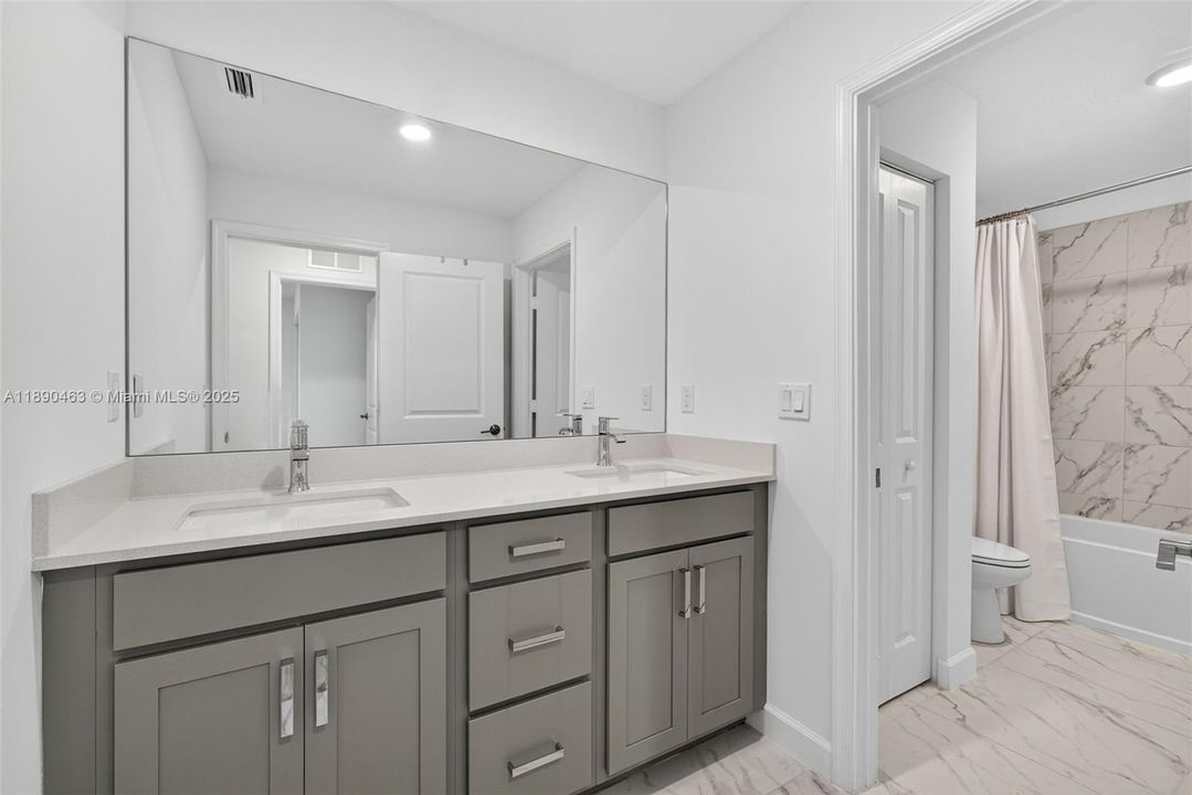 Stylish second full size bathroom with double sinks, quartz counters, and plenty of storage, plus a separate tub/shower area with marble-look tile — perfect for sharing.