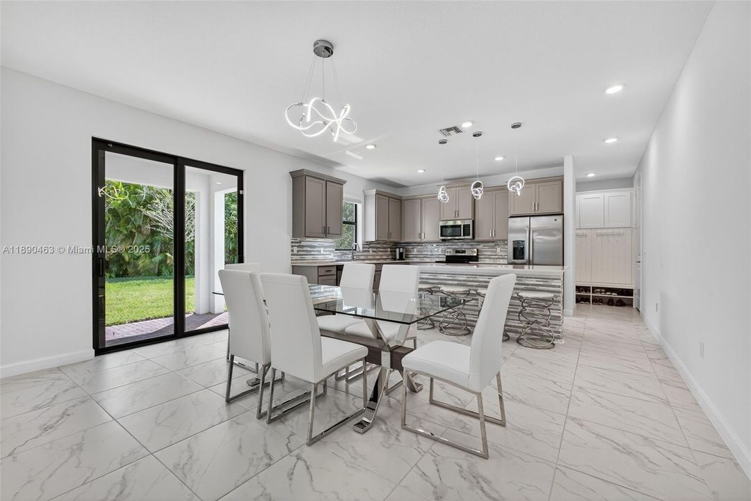 Open dining and kitchen area with sleek tile floors, modern lighting, and a massive island — plus sliding glass doors that lead right out to the backyard and covered patio for easy indoor/outdoor living.