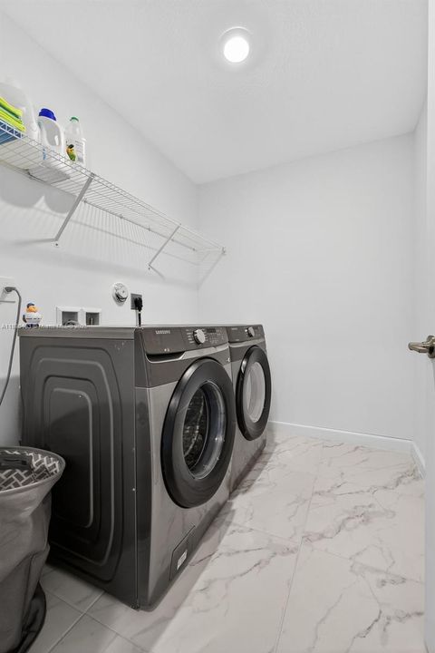Dedicated laundry room with modern front-load washer and dryer, marble-look tile floors, and built-in shelving for easy storage — keeping laundry tucked away and off the main living spaces.