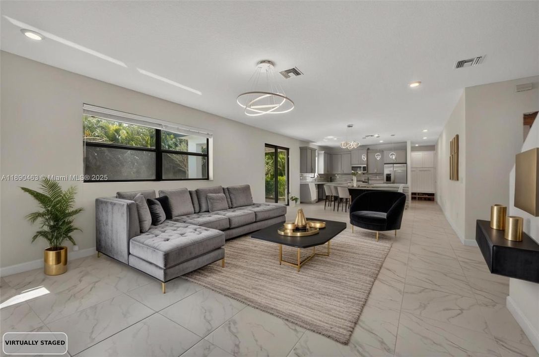 Spacious open-concept living area with modern tile floors, oversized windows for natural light, and direct flow into the dining area and kitchen — plus backyard access right off the living room.