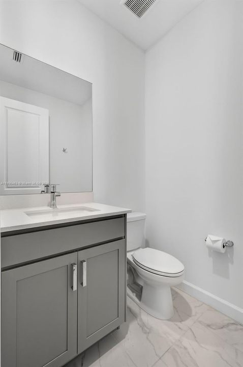 Modern half bath with sleek gray vanity, quartz countertop, and marble-look tile floors — perfect for guests.