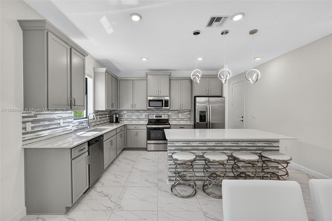 Gorgeous open kitchen with a huge island, stainless steel appliances, modern gray cabinets, and statement lighting — super clean, bright, and perfect for cooking and hosting.
