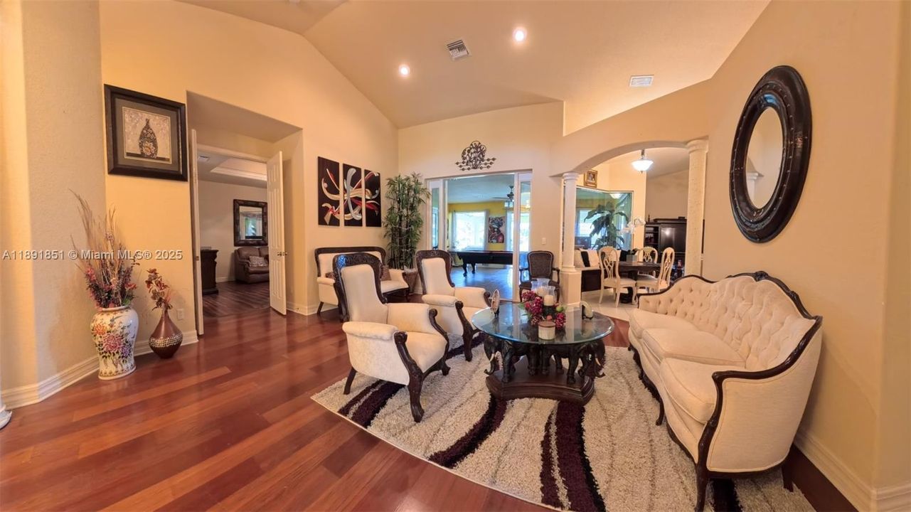 Sitting room with wood flooring, ornate columns/arched walkways lofted ceiling, recessed lighting featuring double entry doors to master suite and French doors leading to game/bonus room.