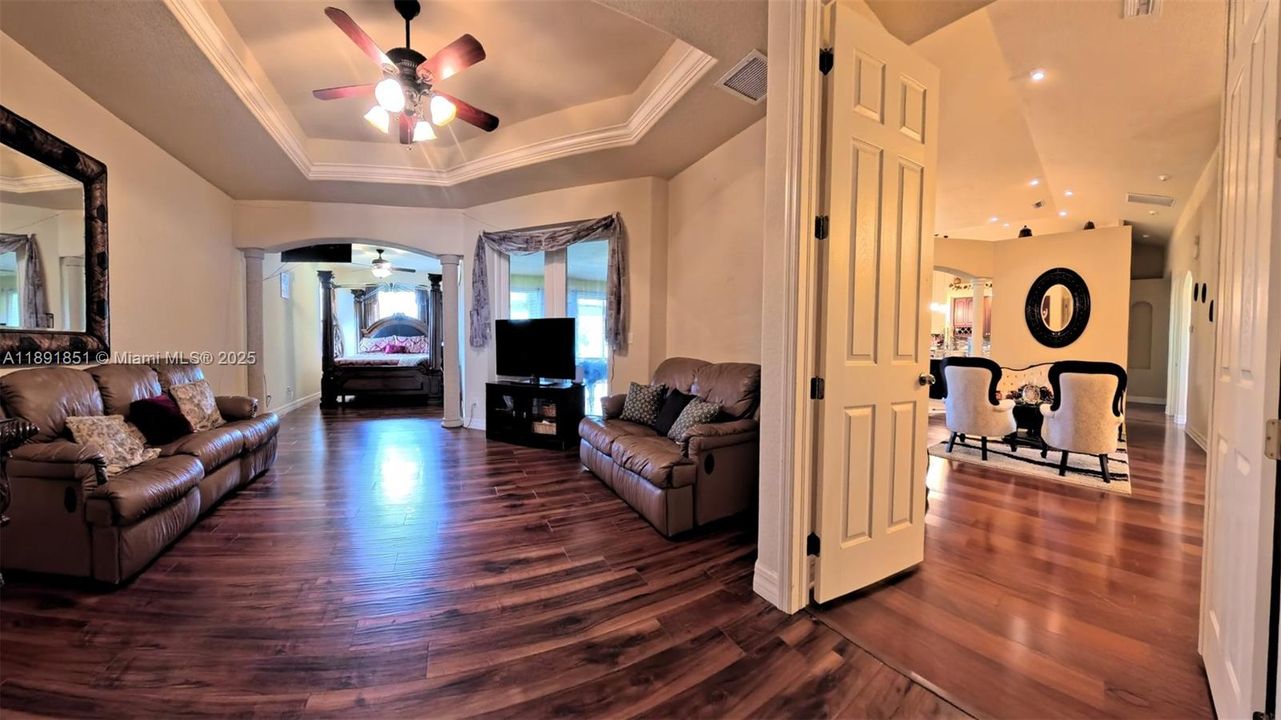 Master bedroom suite with double entry doors and sitting area. Featuring wood floors, ornamental molding, raised ceiling with fan, and decorative columns.