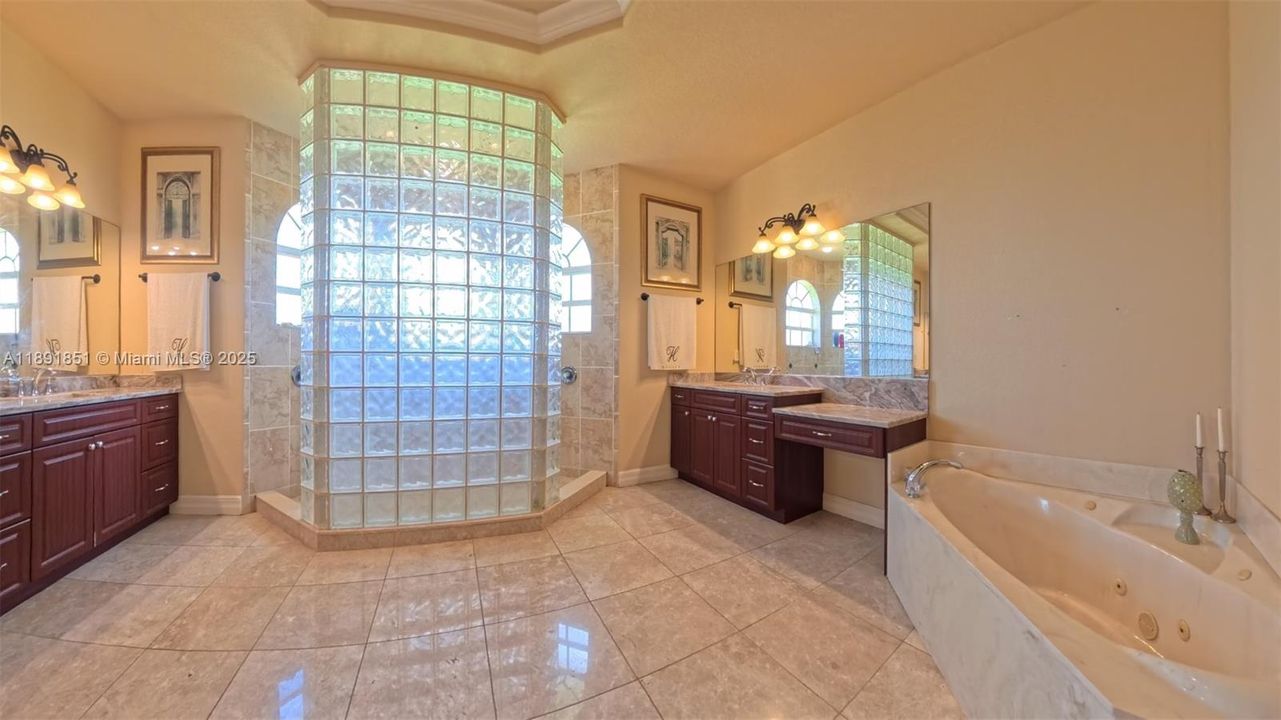 Master bathroom featuring jetted bath tub, double vanities/sinks, walk-through shower with bench, and marble flooring.